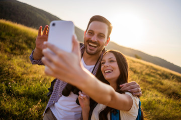 Happy couple is hiking in mountain. They are taking selfie.