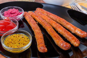 Grilled pork sausages with condiments on black dish close-up