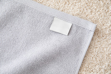 Grey terry towel with white empty label on beige pile carpet.
