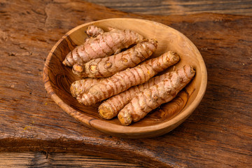 A wooden bowl with whole turmeric roots on a wooden cutting board.