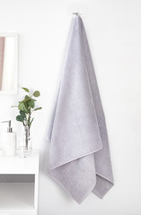 White bathroom interior with hanging grey terry towel, bathroom items and flowers bouquet