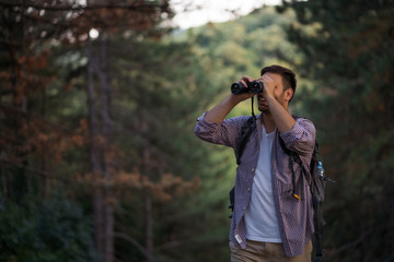 Fototapeta na wymiar Happy adult man is hiking in forest. He is using binoculars.