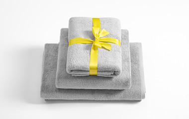 Three folded terry towels tied by yellow ribbon isolated. Stack of grey terry towels against a...