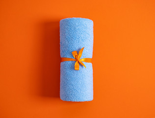 Rolled blue terry towel tie up by ribbon against a orange background.Top view.