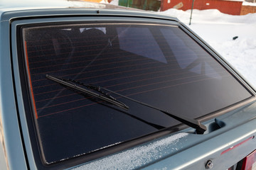 Obraz premium View to the rear window wiper that remove the melted snow and dirt from the windshield of the car during the day during the snow and rain. Auto service and parts.