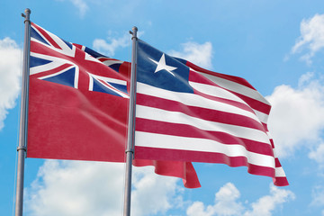 Liberia and Bermuda flags waving in the wind against white cloudy blue sky together. Diplomacy...