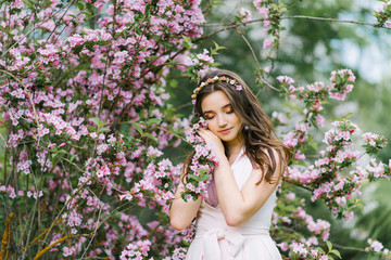 A beautiful romantic girl in a pink delicate dress stands in the spring near a Bush of pink weigela flowers and touches a branch