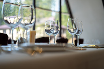 Chic and elegant, gold-plated cutlery and white plates, table setting with empty plates. Glasses in the backlight. Glasses in the light from the window. Side view.