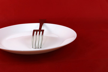 White plate with a fork on a red background.