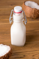 coconut milk in a bottle on a wooden background next to coconut