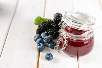 Blueberry and blackberry jam in glass jar, copy space, white wood background