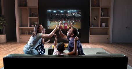A family is watching a basketball moment on the TV and celebrating a goal, sitting on the couch in the living room. The living room is made in 3D.