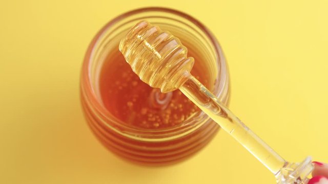 top view hand lift up a honey dipper from a jar and honeu pouring to the jar from spoon