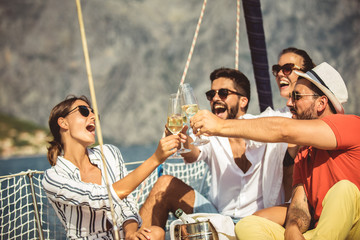 Smiling friends with glasses of champagne on yacht. Focus on glasses. Vacation, travel, sea,...