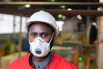 Portrait of Afro-American builder in respirator and hardhat standing at construction site - obrazy, fototapety, plakaty