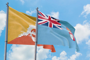 Fiji and Bhutan flags waving in the wind against white cloudy blue sky together. Diplomacy concept, international relations.