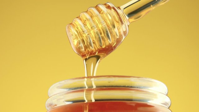 closeup frontal view of honey texture pouring from transparent honey dipper to honey pot