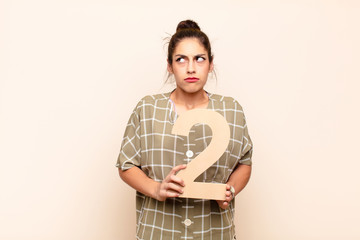 young pretty woman confused, doubtful, thinking, holding a number 2.