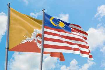 Malaysia and Bhutan flags waving in the wind against white cloudy blue sky together. Diplomacy concept, international relations.