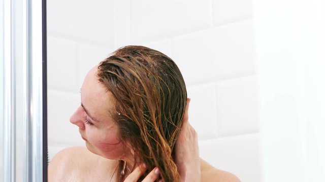 Woman washing hair and body in shower cabine. She is standing wet.