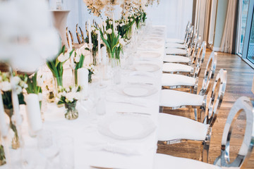 formal luxury elegant wedding decor restaurant tables served white tablecloth, plates, menus, glasses, tulips in vases, orchids, candles silver chairs, blue background