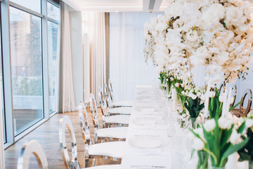 formal luxury elegant wedding decor restaurant tables served white tablecloth, plates, menus, glasses, tulips in vases, orchids, candles silver chairs, blue background