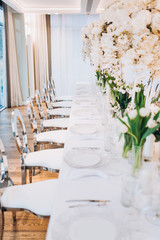 formal luxury elegant wedding decor restaurant tables served white tablecloth, plates, menus, glasses, tulips in vases, orchids, candles silver chairs, blue background