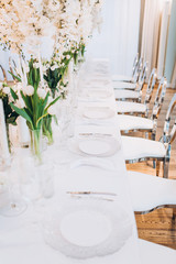 formal luxury elegant wedding decor restaurant tables served white tablecloth, plates, menus, glasses, tulips in vases, orchids, candles silver chairs, blue background