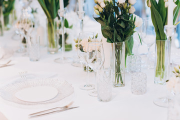 formal luxury elegant wedding decor restaurant tables served white tablecloth, plates, menus, glasses, tulips in vases, orchids, candles silver chairs, blue background