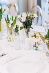 formal luxury elegant wedding decor restaurant tables served white tablecloth, plates, menus, glasses, tulips in vases, orchids, candles silver chairs, blue background