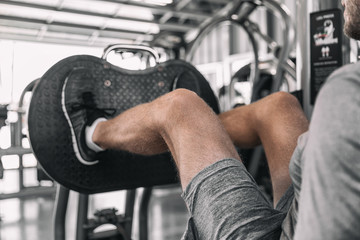 Naklejka na ściany i meble Gym Leg Press machine fit man training legs workout on fitness machine doing heavy weights pushing with hamstring and quads muscles.