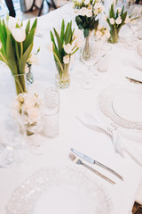 formal luxury elegant wedding decor restaurant tables served white tablecloth, plates, menus, glasses, tulips in vases, orchids, candles silver chairs, blue background
