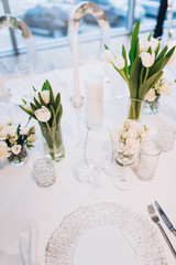 formal luxury elegant wedding decor restaurant tables served white tablecloth, plates, menus, glasses, tulips in vases, orchids, candles silver chairs, blue background