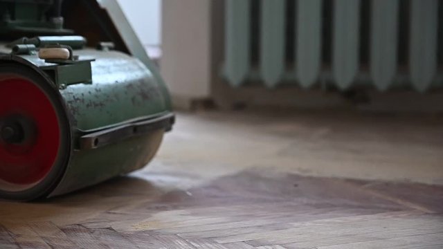 Sanding hardwood floor with the grinding machine. Repair in the apartment. Carpenter doing parquet wood floor polishing maintenance work by grinding machine.Slow motion