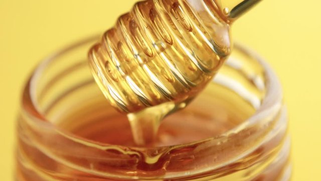 closeup of honey texture, transparent honey dipper with pouring honey on yellow background