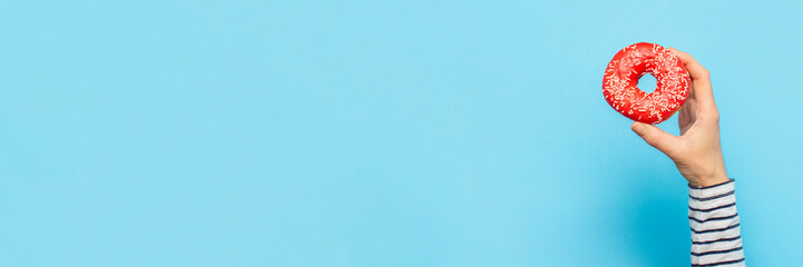 Female hand holds a donut on a blue background. Concept confectionery store, pastries, coffee shop....