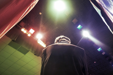 A man in a suit watches from behind the scenes for a performance at a music concert