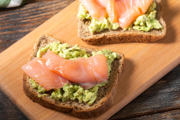 Bruschetta with avocado and salmon on a wooden Board on a brown wooden table. Toasted bread with avocado and red fish. The concept is useful and delicious Breakfast