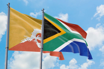 South Africa and Bhutan flags waving in the wind against white cloudy blue sky together. Diplomacy concept, international relations.