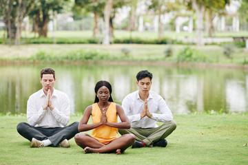 Business people sitting on meadow in park and practicing yoga and lotus position