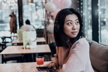 Asian girl alone in the city sits in a cafe and listens to music. Enjoying music in a public place