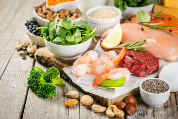 Selection of animal and plant protein sources - fish, meat, beans, cheese, eggs, nuts and seeds, kale, on wood background