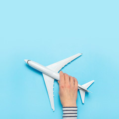 Female hand holds a plane on a blue background. Concept flight, tickets, booking, flight search, travel. Banner. Flat lay, top view