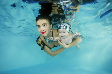 Mom with a little son smiling dives underwater in a swimming pool