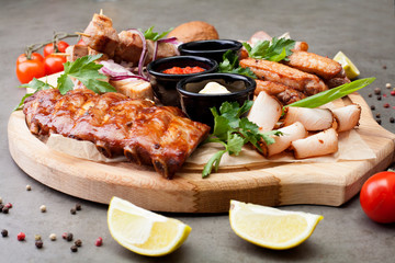 The meat plate is filled with cuts and steaks, supplemented with sauces, decorated with herbs, cherry tomatoes and lemons. The concept of meat or beer appetizer.