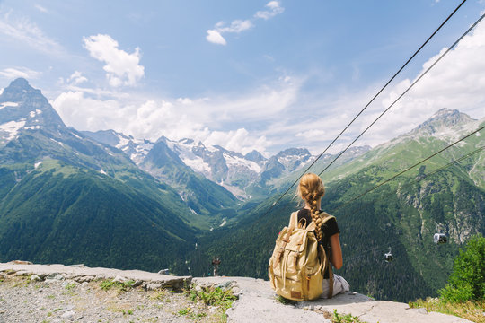 Child traveler sitting on mountain by cableway and enjoying beautiful summer view.