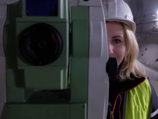 Portrait  of pretty smiling young mining surveyor woman stands by geodetic total station in the...