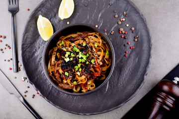 Wok noodles, with shrimp and other Asian ingredients, in a black plate decorated with peas, on a gray background . The concept of Asian cuisine.