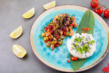 Risotto, rice served on a palm leaf next to a filling of vegetables and meat, on a blue plate, on a gray background, next to lime slices and cherry tomatoes. the concept of recipes or menus for the re