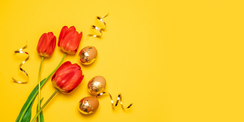 Holiday composition of two red tulips and gold eggs glitter serpentine on a yellow solid background